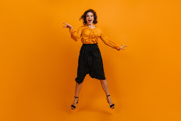 Fototapeta na wymiar Full length view of excited girl in black skirt and trendy blouse. Front view of emotional lady in stylish outfit jumping on yellow background.