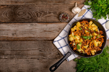 fried chanterelle mushrooms with potatoes onion and parsley in a frying pan and the ingredients on the table. horizontal top view close-up