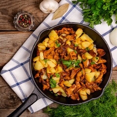 fried chanterelle mushrooms with potatoes onion and parsley in a frying pan and the ingredients on the table. horizontal top view close-up