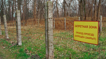 Concrete fence with barbed wire, inscription in Russian language: Forbidden zone, passage is forbidden