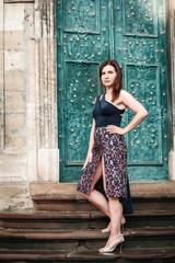 Fototapeta premium Beautiful woman in a sexy dress stands on the stairs on the background of an old house. Copy, empty space for text