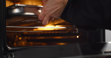 Close up of chef putting tray with meal in oven cooking dinner