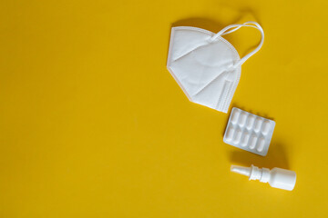 FFP3 mask, nasal drops, thermometer, tablets, various medicines lie on the table, top view, on a yellow background