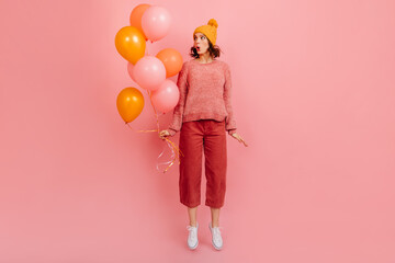 Full length view of woman in yellow hat holding air balloons. Studio shot of atttactive girl posing at party. - obrazy, fototapety, plakaty