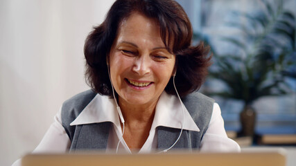 Portrait of senior businesswoman in earphones having video conference on laptop
