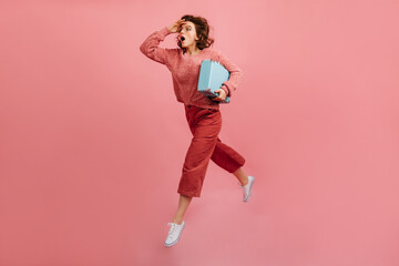 Stressed woman with valise hurrying on pink background. Studio shot of running lady with suitcase.
