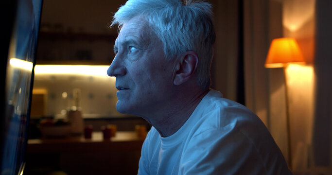 Side View Of Old Man Sitting Near Large Screen And Watching Tv.