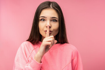Photo of attractive young woman shows gesture not loud silence, wears casual pink t-shirt white isolated pink color background