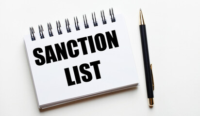 On a light background, a white notebook with the words SANCTION LIST and a pen.