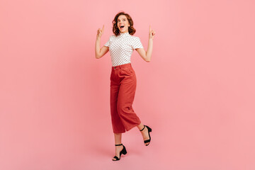 Gorgeous girl in black shoes dancing in studio. Glad curly lady pointing with fingers up.