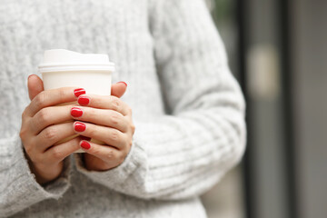 female hand holding paper cup of take away drinking coffee on city background. space place for your text or logo.