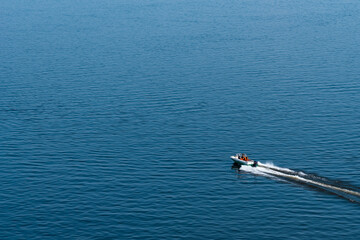 Fast small boat sails on the blue water surface, leaving a trail of foam