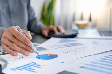 Finance business people or accountants point to the graph and use a calculator to calculate company income, expenses, taxes, and employee bonuses for Next year's improvement plan