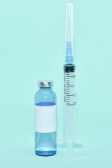 Medical ampoule (vial) with vaccine and syringe on light blue background. White label on bottle, space for text. vaccination against covid-19, flu. Cosmetological injections. COVID-19 vaccine vial