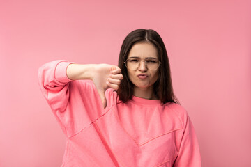 Photo of attractive woman in glasses disappointed, disagree and dislike for something, wear casual pink t-shirt white pants isolated pink color background