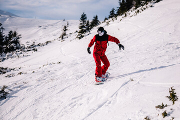 Fototapeta na wymiar A guy in a red jumpsuit eating freeride on a snowboard on a snowy slope