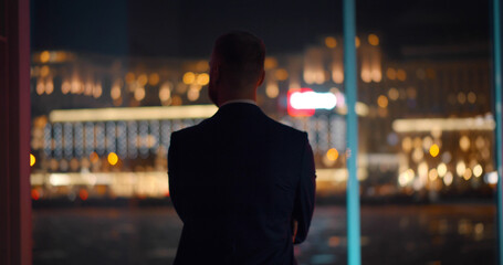 Back view of successful young businessman in suit is looking out of panoramic window.