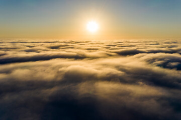Striking aerial view of the sunset sky with the clouds below us. The shadows projected from the Sun passing through the clouds create a dramatical landscape view. Flying above the clouds in the search