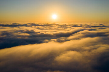 Striking aerial view of the sunset sky with the clouds below us. The shadows projected from the Sun passing through the clouds create a dramatical landscape view. Flying above the clouds in the search