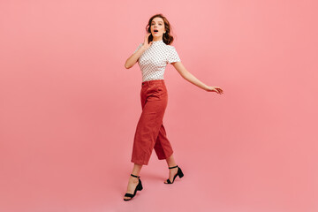 Fototapeta na wymiar Excited woman in white t-shirt gesturing in front of camera. Studio shot of charming girl in pink pants.