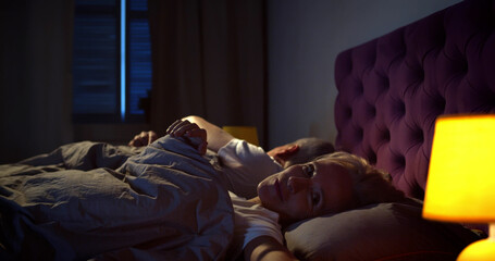 Senior couple saying good night and turning off lights falling asleep in bed