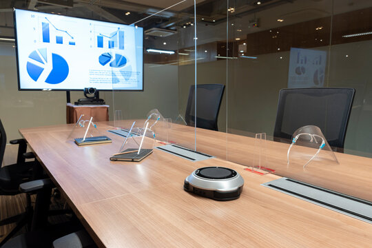 Video conference meeting room with clear acrylic sheet separates the center on the conference table to prevent COVID-19 and face shield on the table. 
