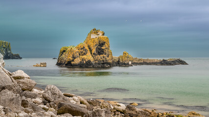 Fototapeta premium Big Rock overgrown with green and yellow moss and seaweed in green ocean under dark sky in Donegal, Ireland
