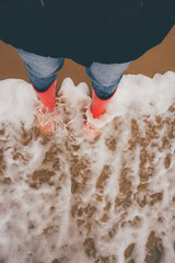 Woman weared red rubber Boots on the water on the seaside, stormy day.