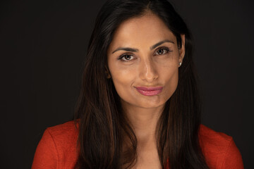 Headshot of a beautiful Asian Indian woman in an orange sweater. 