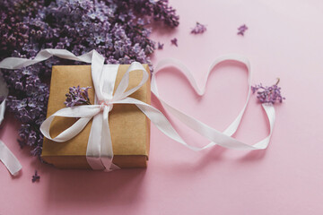 Happy valentines day and mothers day. Lilac flowers, gift box and heart ribbon on pink paper