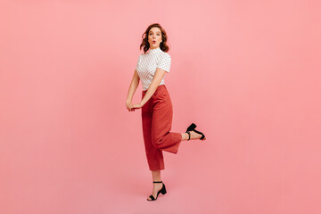 Full length view of woman in bright pants standing on one leg. Studio shot of happy curly girl.