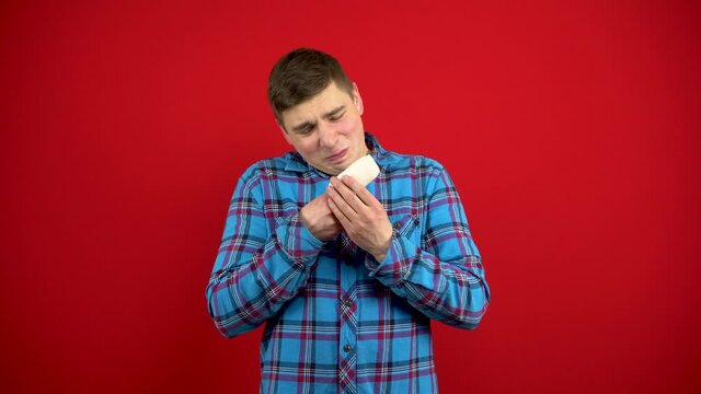 The young man's index finger is bandaged and sore. Shooting on a red background.