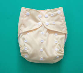 Reusable cloth baby diaper. Eco friendly nappy yellow color on green background.