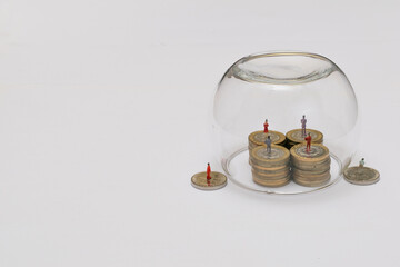 Miniatures of people on a pile of coins protected by glass bubble