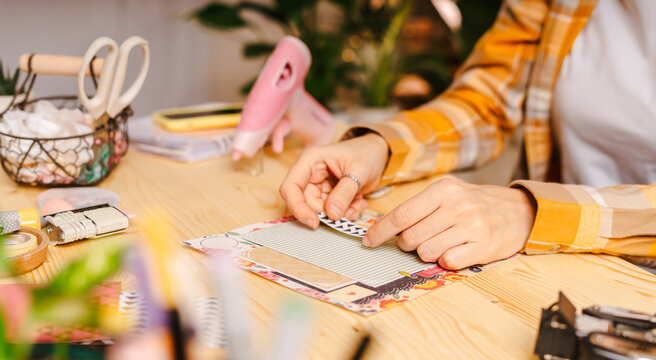 Cropped shot of women making homemade scrapbooking album from paper. DIY, hobby concept, gift idea, decor with handcraft attributes, home production, the process of creation, creativity.