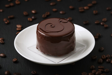 Austrian cake, sackertorte. Chocolate cake on a white plate. Coffee beans on a black textured table. Side view of a chocolate dessert.