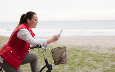 Attractive mature woman on bicycle using mobile phone beach background