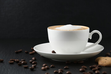 Coffee beans on the table. White cup with cappuccino on a black table, white background. Cookies and coffee.