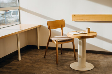 Table and chair at an empty cafe in sun light, with an opened notebook and a cup of coffee.