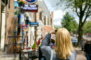 Young woman takes pictures in vacation spent in Amsterdam with beautiful architecture and coffee shop.