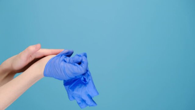 Close up of unrecognizable young female removes medical protective gloves and throw it in trash, isolated on blue studio background with copy space for advertisement. Concept end of virus epidemic