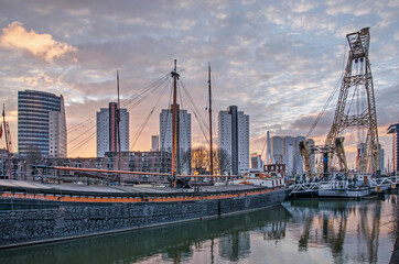 Fototapeta premium Rotterdam, The Netherlands, January 13, 2021: spectacular sky at sunrise over Leuvehaven harbour with historic barges and maritime equipment