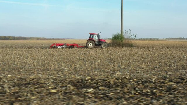 Low dolly move in aerial view of tractor as dragging a disc harrow over agricultural field, farmland