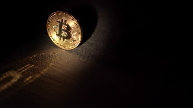 Shiny bitcoin rotating and reflecting light, on a wooden surface. blockchain
