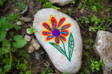 Pebbles with a painted flower on the background of a cooperative and community ecological garden....