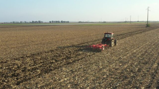 Above view shot of tractor, he is pulling machine, harrowing arable field, preparing soil for planting new crop next season.