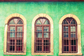 Fototapeta na wymiar Three vaulted windows with bars on the green wall