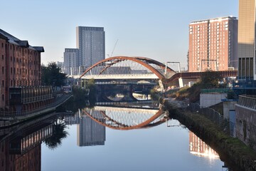 Ordsall Chord bridge over the river Irwell in Manchester City centre with modern buildings and reflections in the water. 