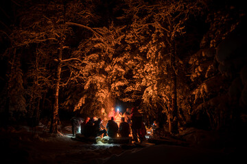 People in the winter night forest around a campfire - obrazy, fototapety, plakaty