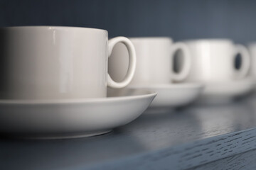 white porcelain teacups and saucers stand on a shelf with a wooden texture in blue-gray close-up